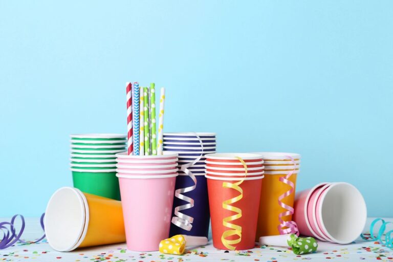 Colorful paper cups with straws and confetti on blue background